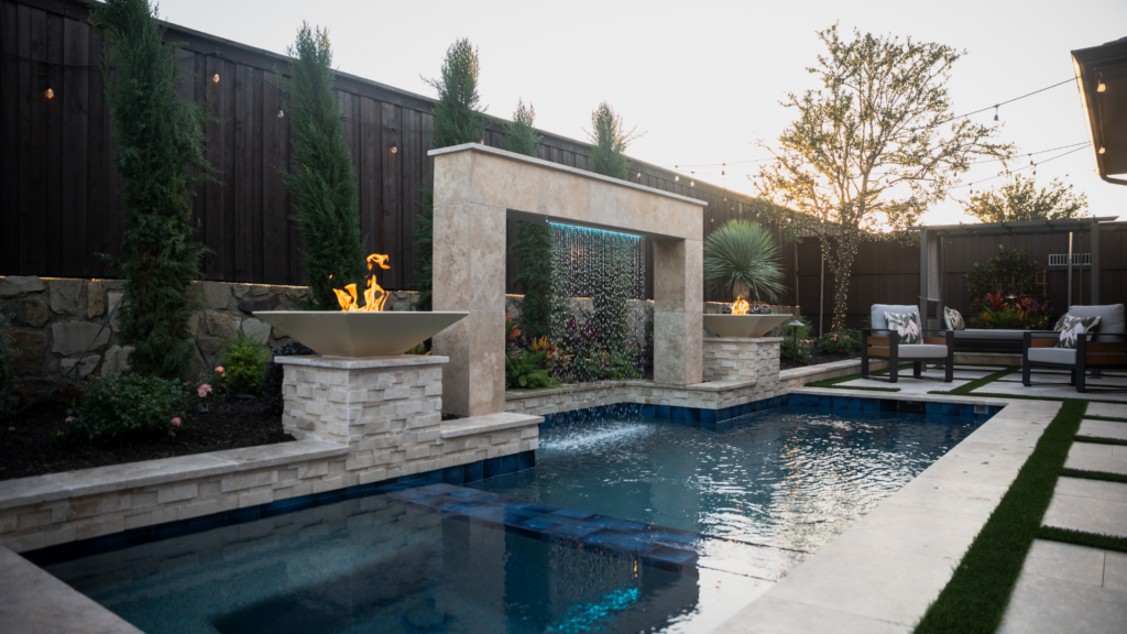 "Modern backyard pool with stone waterfall, fire bowls, and landscaped seating area."
