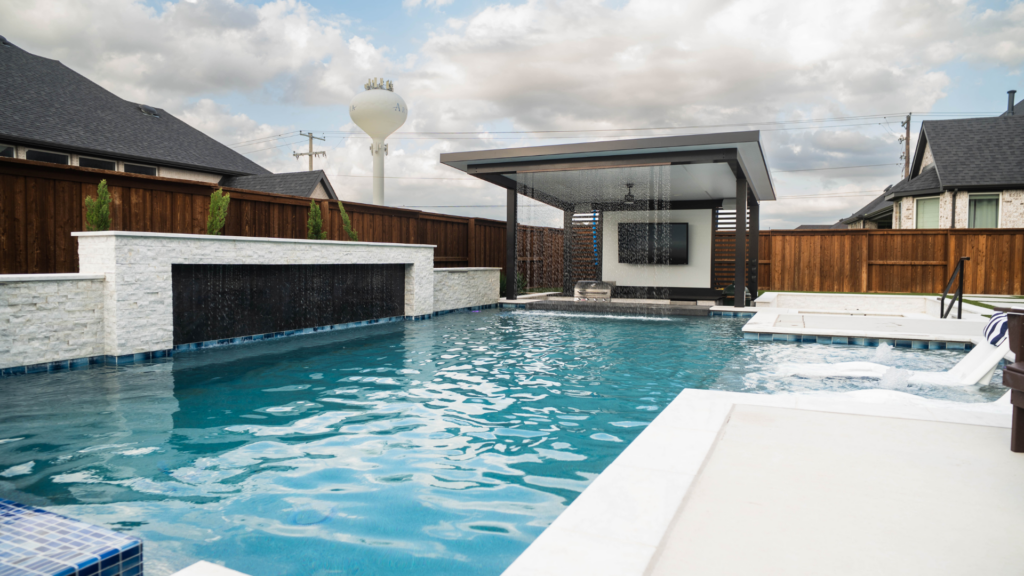 "Modern backyard pool with waterfall wall, covered pavilion, and in-pool lounge chairs."