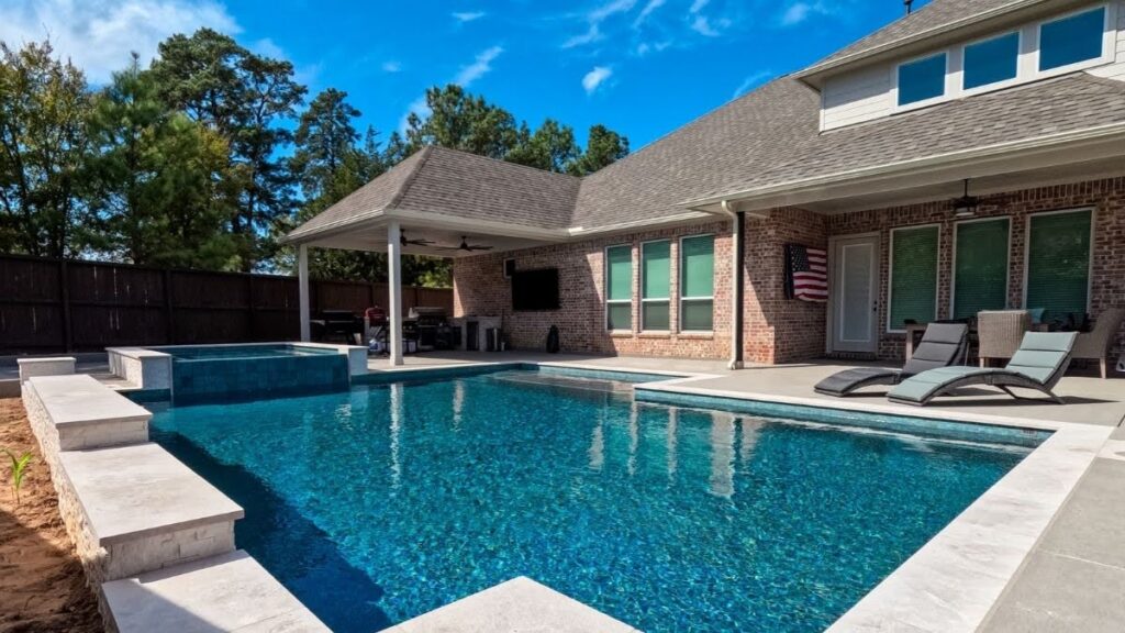 "Custom pool with attached spa and stone coping behind a brick new build home with a covered patio and outdoor kitchen"