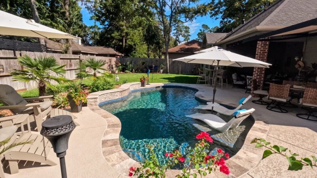 "Backyard swimming pool with in-pool lounge chairs, stone ledge, patio umbrella, and covered seating area."