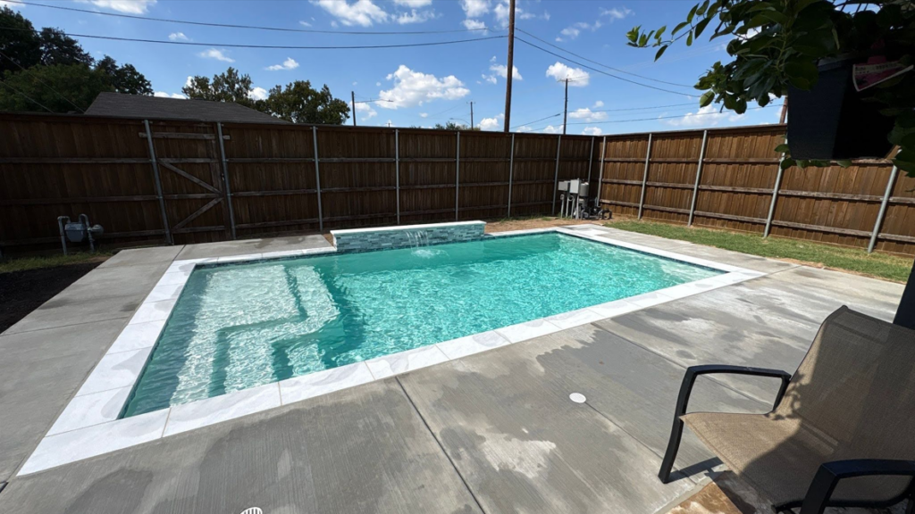 "Rectangular inground pool with tanning ledge and water feature, concrete decking, wood privacy fence"
